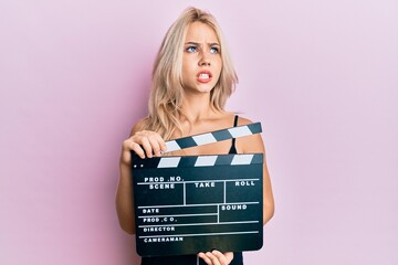 Sticker - Beautiful caucasian blonde girl holding video film clapboard angry and mad screaming frustrated and furious, shouting with anger looking up.