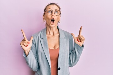 Wall Mural - Beautiful caucasian woman wearing business jacket and glasses amazed and surprised looking up and pointing with fingers and raised arms.