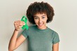 © Krakenimages.com - Young hispanic girl holding support green ribbon looking positive and happy standing and smiling with a confident smile showing teeth