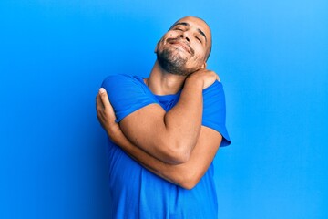 Poster - Hispanic adult man wearing casual blue t shirt hugging oneself happy and positive, smiling confident. self love and self care