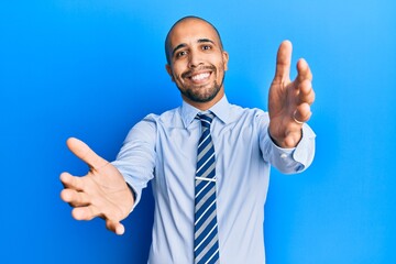 Sticker - Hispanic adult man wearing business shirt and tie looking at the camera smiling with open arms for hug. cheerful expression embracing happiness.