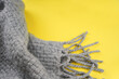 Gray knitted scarf with fringe on yellow background. Colors of the Year 2021 concept. Top view, copy space