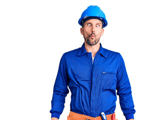 Poster - Young handsome man wearing worker uniform and hardhat making fish face with lips, crazy and comical gesture. funny expression.