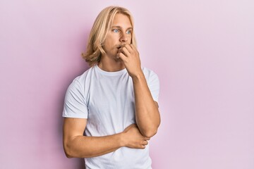 Caucasian young man with long hair wearing casual white t shirt looking stressed and nervous with hands on mouth biting nails. anxiety problem.