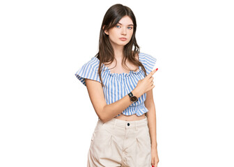 Sticker - Young beautiful caucasian girl wearing casual clothes pointing with hand finger to the side showing advertisement, serious and calm face