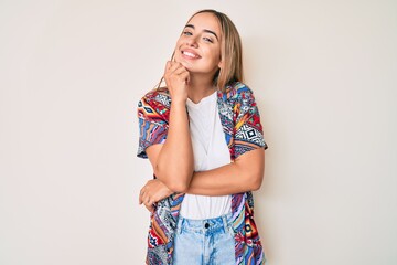 Wall Mural - Young beautiful blonde woman wearing modern clothes looking confident at the camera with smile with crossed arms and hand raised on chin. thinking positive.