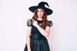 © Krakenimages.com - Young beautiful woman wearing witch halloween costume pointing with hand finger to the side showing advertisement, serious and calm face