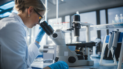 Wall Mural - in bright medical science laboratory: beautiful microbiologist looks under microscope does analysis 