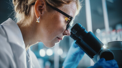 Wall Mural - in bright medical science laboratory: beautiful microbiologist wearing glasses looks under microscop