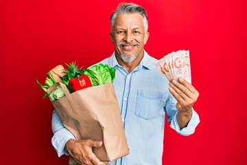 Wall Mural - Middle age grey-haired man holding groceries and singapore dollars banknotes smiling with a happy and cool smile on face. showing teeth.