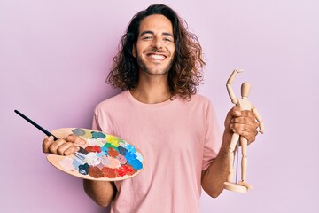 Sticker - Young handsome man with long hair holding painter palette and art manikin smiling with a happy and cool smile on face. showing teeth.