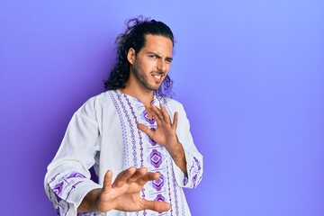 Sticker - Young handsome man with long hair wearing bohemian and hippie shirt disgusted expression, displeased and fearful doing disgust face because aversion reaction. with hands raised