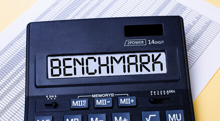 A calculator labeled BENCHMARK is on the table near the report. Financial concept