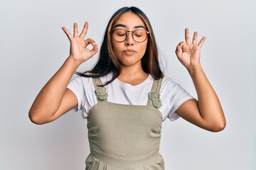 Young latin woman wearing casual clothes and glasses relax and smiling with eyes closed doing meditation gesture with fingers. yoga concept.