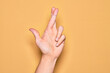 Hand of caucasian young man showing fingers over isolated yellow background gesturing fingers crossed, superstition and lucky gesture, lucky and hope expression