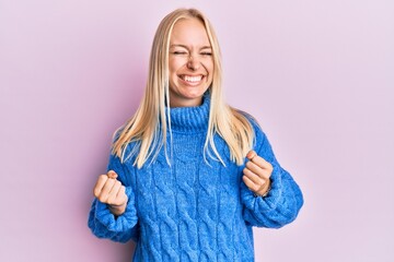 Canvas Print - Young blonde girl wearing wool winter sweater excited for success with arms raised and eyes closed celebrating victory smiling. winner concept.