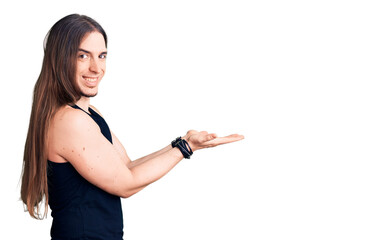 Young adult man with long hair wearing goth style with black clothes pointing aside with hands open palms showing copy space, presenting advertisement smiling excited happy