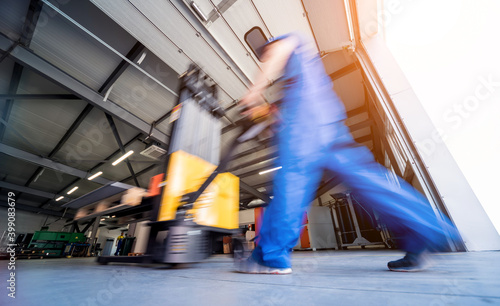 Fotografie, Obraz A worker in a warehouse uses a hand pallet stacker to transport pallets