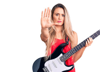 Canvas Print - Young beautiful blonde woman playing electric guitar with open hand doing stop sign with serious and confident expression, defense gesture