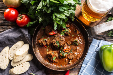 Hungarian goulash in a bowl with bell pepper, tomatoes, herbs, dumplings and a draft beer