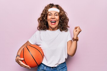 Sticker - Middle age brunette basketball player woman holding game ball over isolated pink background screaming proud, celebrating victory and success very excited with raised arm