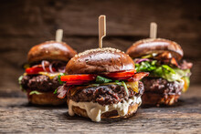 Assortment Of Three Various Burgers Ready To Be Plated, With A Dark Wooden Background