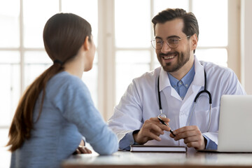 Happy young Caucasian male GP or physician in white medical uniform have consultation with female patient in private hospital. Smiling man doctor consult woman client at meeting in clinic.