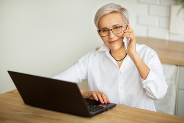 Wall Mural - beautiful stylish female aged with a mobile phone at a table with a laptop