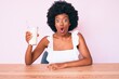 © Krakenimages.com - Young african american woman holding glass of milk scared and amazed with open mouth for surprise, disbelief face