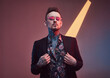 © Fxquadro - Weared with sunglasses stylish and tattooed businessperson with fashionable haircut and beard poses in dark and colourful background with lights.