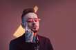 © Fxquadro - Serious and tattooed hipster businessperson with beard and stylish haircut poses in dark room with lights and colourful walls touching his face with finger.