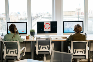 Wall Mural - Rear view of male and female operators sitting in front of computer monitors