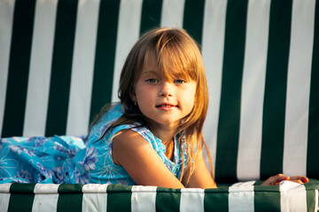 Wall Mural - Portrait of little girl lying on a swing in the yard of a country house.