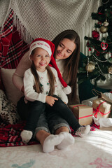 Wall Mural - Smiling Mother and daughter with presents and Christmas decorations in the background. Christmas family presents concept. 