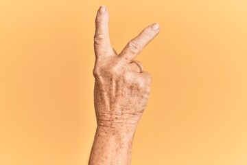 senior caucasian hand over yellow isolated background counting number 2 showing two fingers, gesturi