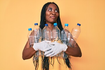 Sticker - African american woman with braids holding recycling plastic bottles smiling looking to the side and staring away thinking.