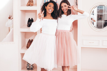 Two young beautiful smiling international hipster female in trendy summer dresses. Sexy carefree women posing in pink wardrobe. Positive models having fun. Concept of friendship