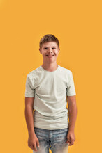 Portrait Of Cheerful Teenaged Disabled Boy With Down Syndrome Smiling At Camera While Standing Isolated Over Yellow Background