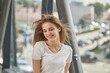 © Evgenia - A young woman with long blond hair is smiling. Hair flying in the wind. Bridge with iron pipes.