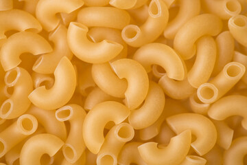 Close up above top view photo of elbow shaped yellow uncooked macaroni textured background