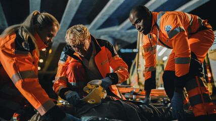 Team of EMS Paramedics Provide Help to an Injured Young Man. Doctor in Gloves Attaches Cervical Neck Collar on a Patient. Emergency Care Assistants Arrived in an Ambulance Vehicle at Night.