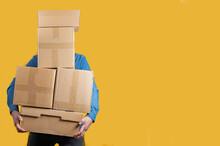 Courier In A Blue Denim Shirt With Boxes In His Hands On A Yellow Background