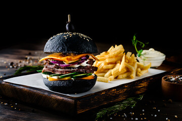 Canvas Print - Black burger with french fries on wooden cutting board on black background