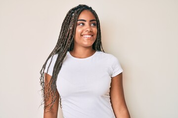 Wall Mural - Young african american woman with braids wearing casual white tshirt looking away to side with smile on face, natural expression. laughing confident.