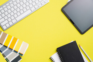 Graphic designer workspace top view with tablet, computer keyboard, RAL color palette, notebook on yellow background. Flat lay, overhead. Creative professional office desk.