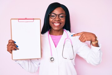 Young african american woman wearing doctor stethoscope holding clipboard pointing finger to one self smiling happy and proud