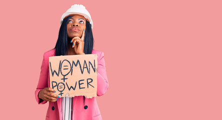 Poster - Young african american woman wearing architect helmet holding woman power banner serious face thinking about question with hand on chin, thoughtful about confusing idea