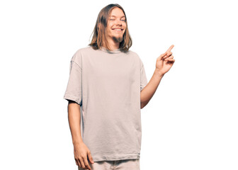 Handsome caucasian man with long hair wearing casual clothes with a big smile on face, pointing with hand and finger to the side looking at the camera.