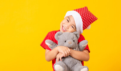 Portrait of Asian little boy smiling hugging teddy bear, Kid dressed in Santa Claus hat the concept of Christmas Xmas day, studio shot isolated on yellow background with copy space for text