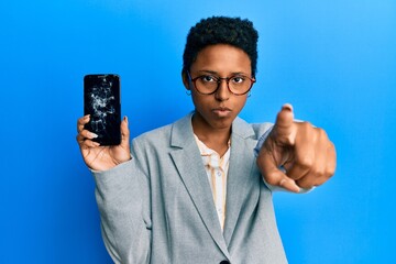 Wall Mural - Young african american girl holding broken smartphone showing cracked screen pointing with finger to the camera and to you, confident gesture looking serious